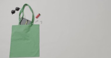 Güneş gözlüklü yeşil çanta, defter, beyaz arka planda ruj, kopyalama alanı, yavaş çekim. Moda, tasarım ve kumaş.