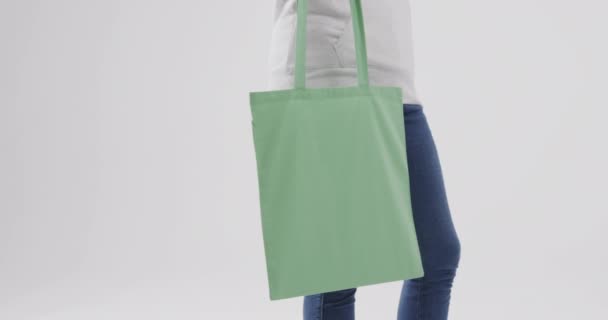 白人女性は白い背景に緑の袋を保持し 白いパーカーを着て コピースペース スローモーション ファッション デザイン ファブリック — ストック動画