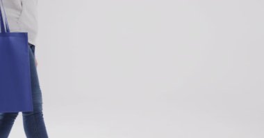 Beyaz kapüşonlu beyaz kadın beyaz arka planda mavi çanta tutuyor. Kopya alanı, ağır çekim. Moda, tasarım, kıyafetler ve kumaş.