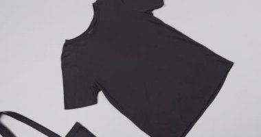 Siyah çantayı ve beyaz arka plandaki tişörtü kapatın, fotokopi alanı olan, yavaş çekim. Moda, tasarım, kıyafetler ve kumaş.