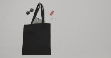 Güneş gözlüklü siyah çanta, defter, beyaz arka planda ruj, kopyalama alanı, yavaş çekim. Moda, tasarım ve kumaş.