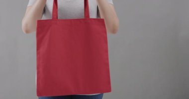 Beyaz tişört giyen beyaz kadın gri arka planda kırmızı çanta tutuyor, fotokopi alanı, ağır çekim. Moda, tasarım, kıyafetler ve kumaş.