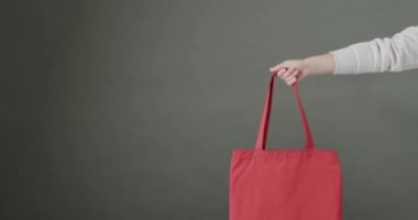 Beyaz bir kadının elinde gri arka planda kırmızı çanta var. Kopya alanı, ağır çekim. Moda, tasarım ve kumaş.