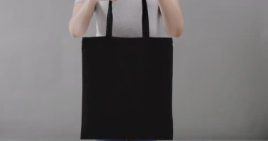 Beyaz tişört giyen beyaz kadın gri arka planda siyah çanta tutuyor, fotokopi alanı, ağır çekim. Moda, tasarım, kıyafetler ve kumaş.