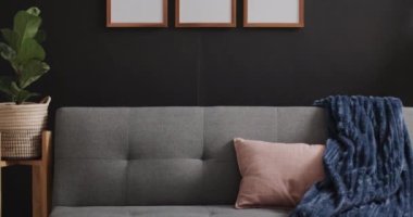 Beyaz arka planda fotokopi alanı olan üç tahta çerçeve, kanepe, bitki ve siyah duvar. Çerçeve, ev dekorasyonu ve iç tasarım konsepti.