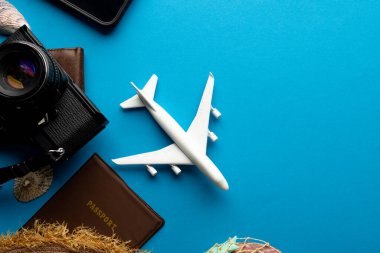 Uçak modeli, pasaport ve kamera mavi arka planda fotokopi alanı var. Seyahat, ulaşım ve tatil.