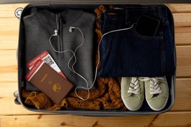 Giysiler, ayakkabılar, pasaport, biletler, ahşap arka planda akıllı telefon ve kulaklıklar. Seyahat ve tatil.