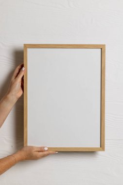 Dikey olarak beyaz duvara karşı boş ahşap çerçeve ve kopya alanı tutan eller. Çerçeve şablonu, iç tasarım ve dekorasyonu düzenle.