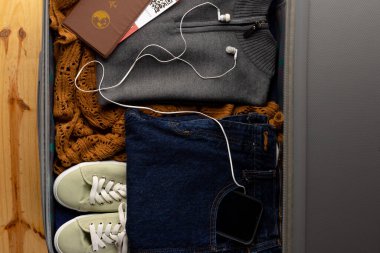 Giysiler, ayakkabılar, pasaport, biletler, ahşap arka planda akıllı telefon ve kulaklıklar. Seyahat ve tatil.