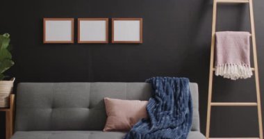 Beyaz arka planda fotokopi alanı olan üç tahta çerçeve, kanepe, bitki ve siyah duvar. Çerçeve, ev dekorasyonu ve iç tasarım konsepti.