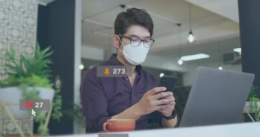Ofiste akıllı telefon kullanarak yüz maskesi takan Asyalı adamın sosyal medya simgelerinin animasyonu. Sosyal medya ağı ve covid-19 salgın konsepti