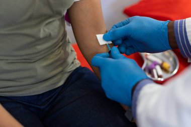 Afrika kökenli Amerikalı erkek doktor ve melez kadın hasta doktorun ofisinde kan koleksiyonu yapıyor. Hastane, ilaç ve sağlık hizmetleri.