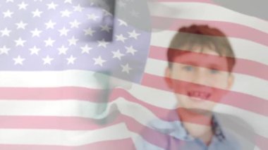 Sınıfta gülümseyen beyaz bir çocuğun üzerine Amerikan bayrağının dalgalanması. Okul, Amerikan eğitimi, çocukluk ve öğrenme, dijital olarak üretilen video.