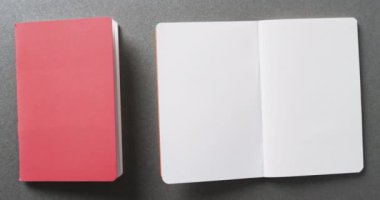 Açık boş kitabı ve arka planı gri olan pembe kitabı yavaş çekimde kapat. Edebiyat, okuma ve kitaplar.