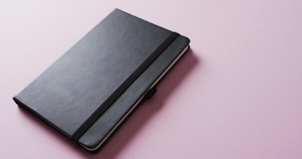 Close Van Gesloten Zwarte Notebook Met Kopieerruimte Roze Achtergrond Slow — Stockvideo