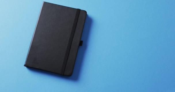 Nahaufnahme Eines Geschlossenen Schwarzen Notizbuchs Mit Kopierraum Auf Blauem Hintergrund — Stockvideo