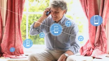 Evde cep telefonuyla konuşan kıdemli beyaz adamın üzerine bağlı ikonların animasyonu. Dijital bileşik, çoklu pozlama, iletişim, emeklilik, sohbet ve teknoloji kavramı.