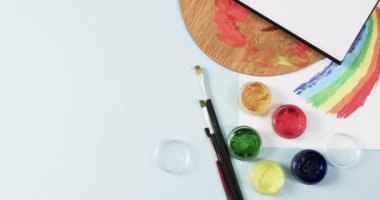 Defterin yukarıdan görünüşü, fırçalar ve boyalar mavi arka planda, yavaş çekimde. Kırtasiye, yaratıcılık, öğrenme, okul ve eğitim kavramı.