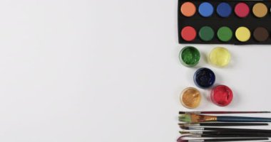 Boyaların ve fırçaların beyaz arkaplandaki görünümü fotokopi alanı ile yavaş çekimde. Kırtasiye, yaratıcılık, öğrenme, okul ve eğitim kavramı.