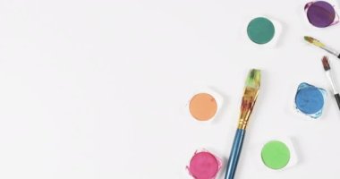 Boyaların ve fırçaların beyaz arkaplandaki görünümü fotokopi alanı ile, yavaş çekimde. Kırtasiye, yaratıcılık, öğrenme, okul ve eğitim kavramı.