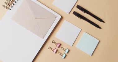 Bej arka planda yavaş çekimde dizilmiş defter, kalem ve kırtasiye malzemelerinin genel görünümü. Masa, iletişim, çalışma alanı, kırtasiye ve düzen kavramı.