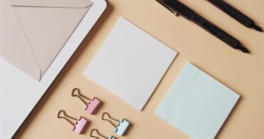 Bej arka planda yavaş çekimde dizilmiş defter, kalem ve kırtasiye malzemelerinin genel görünümü. Masa, iletişim, çalışma alanı, kırtasiye ve düzen kavramı.