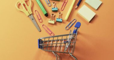 Turuncu arka planda alışveriş arabaları ve okul eşyalarının genel görünümü. Kırtasiye, yaratıcılık, öğrenme, okul ve eğitim kavramı.