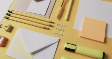 Kalemleri, kâğıtları ve kâğıtları sarı arka planda yavaş çekimde kapat. Masa, iletişim, çalışma alanı, kırtasiye ve düzen kavramı.