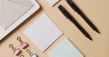 Bej arka planda yavaş çekimde dizilmiş defter, kalem ve kırtasiye malzemelerinin genel görünümü. Masa, iletişim, çalışma alanı, kırtasiye ve düzen kavramı.