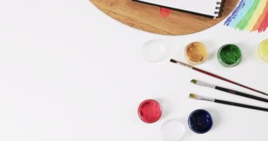 Not defterinin yukarıdan görünüşü, beyaz arka planda fırçalar ve boyalar fotokopi alanı ile, yavaş çekimde. Kırtasiye, yaratıcılık, öğrenme, okul ve eğitim kavramı.