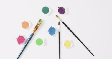 Boyaların ve fırçaların beyaz arkaplandaki görünümü fotokopi alanı ile, yavaş çekimde. Kırtasiye, yaratıcılık, öğrenme, okul ve eğitim kavramı.