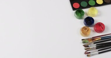 Boyaları ve fırçaları beyaz arkaplanda fotokopi alanı ile yavaş çekimde kapat. Kırtasiye, yaratıcılık, öğrenme, okul ve eğitim kavramı.