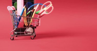 Okul eşyalarıyla alışveriş arabasını kapat ve kırmızı arka planda fotokopi alanı olan boyaları. Kırtasiye, yaratıcılık, öğrenme, okul ve eğitim kavramı.