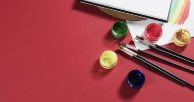 Not defterini kapat, kırmızı arkaplanda fotokopi alanı ile yavaş çekimde boya ve fırçalar. Kırtasiye, yaratıcılık, öğrenme, okul ve eğitim kavramı.