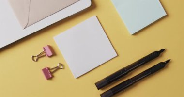 Ağır çekimde sarı arka planda dizilmiş defter, kalem ve kırtasiye malzemelerinin genel görünümü. Masa, iletişim, çalışma alanı, kırtasiye ve düzen kavramı.