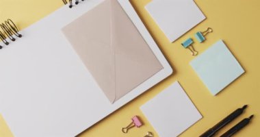 Ağır çekimde sarı arka planda dizilmiş defter, kalem ve kırtasiye malzemelerinin genel görünümü. Masa, iletişim, çalışma alanı, kırtasiye ve düzen kavramı.