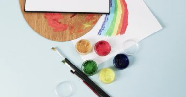 Not defterinin yukarıdan görünüşü, mavi arka planda fırçalar ve boyalar fotokopi alanı ile, yavaş çekimde. Kırtasiye, yaratıcılık, öğrenme, okul ve eğitim kavramı.