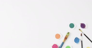 Boyaların ve fırçaların beyaz arkaplandaki görünümü fotokopi alanı ile, yavaş çekimde. Kırtasiye, yaratıcılık, öğrenme, okul ve eğitim kavramı.