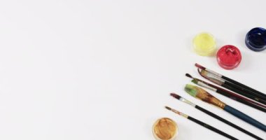 Boyaların ve fırçaların beyaz arkaplandaki görünümü fotokopi alanı ile, yavaş çekimde. Kırtasiye, yaratıcılık, öğrenme, okul ve eğitim kavramı.