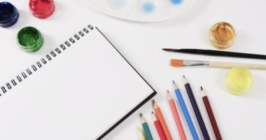 Defteri, boyaları, fırçaları ve pastel boyaları beyaz arka planda yavaş çekimde kapat. Kırtasiye, yaratıcılık, öğrenme, okul ve eğitim kavramı.