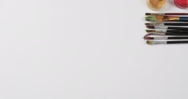 Boyaların ve fırçaların beyaz arkaplandaki görünümü fotokopi alanı ile yavaş çekimde. Kırtasiye, yaratıcılık, öğrenme, okul ve eğitim kavramı.