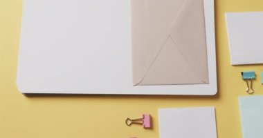 Ağır çekimde sarı arka planda dizilmiş defter, kalem ve kırtasiye malzemelerinin genel görünümü. Masa, iletişim, çalışma alanı, kırtasiye ve düzen kavramı.