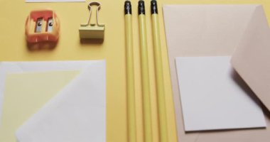 Kalemleri, kâğıtları ve kâğıtları sarı arka planda yavaş çekimde kapat. Masa, iletişim, çalışma alanı, kırtasiye ve düzen kavramı.