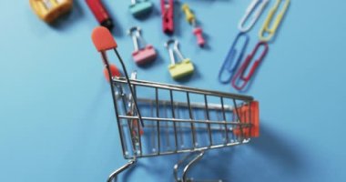 Mavi arka planda alışveriş arabasının ve okul eşyalarının genel manzarası. Kırtasiye, yaratıcılık, öğrenme, okul ve eğitim kavramı.