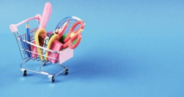 Okul eşyalarıyla alışveriş arabalarını kapatın ve mavi arka planda yer açın. Kırtasiye, yaratıcılık, öğrenme, okul ve eğitim kavramı.