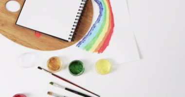 Not defterinin yukarıdan görünüşü, beyaz arka planda fırçalar ve boyalar fotokopi alanı ile, yavaş çekimde. Kırtasiye, yaratıcılık, öğrenme, okul ve eğitim kavramı.