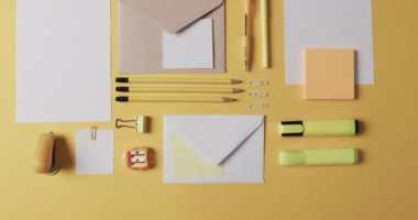 Kalemlerin, kalemlerin ve kırtasiyelerin yukarıdan görünüşü sarı arka planda, yavaş çekimde. Masa, iletişim, çalışma alanı, kırtasiye ve düzen kavramı.