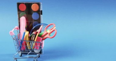 Okul eşyalarıyla alışveriş arabalarını kapatın ve mavi arka planda fotokopi alanı olan boyaları. Kırtasiye, yaratıcılık, öğrenme, okul ve eğitim kavramı.