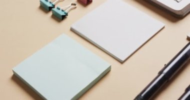 Not defterini, kalemleri ve kâğıtları bej arka planda yavaş çekimde kapat. Masa, iletişim, çalışma alanı, kırtasiye ve düzen kavramı.