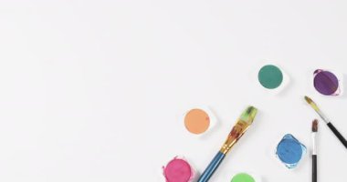 Boyaların ve fırçaların beyaz arkaplandaki görünümü fotokopi alanı ile, yavaş çekimde. Kırtasiye, yaratıcılık, öğrenme, okul ve eğitim kavramı.